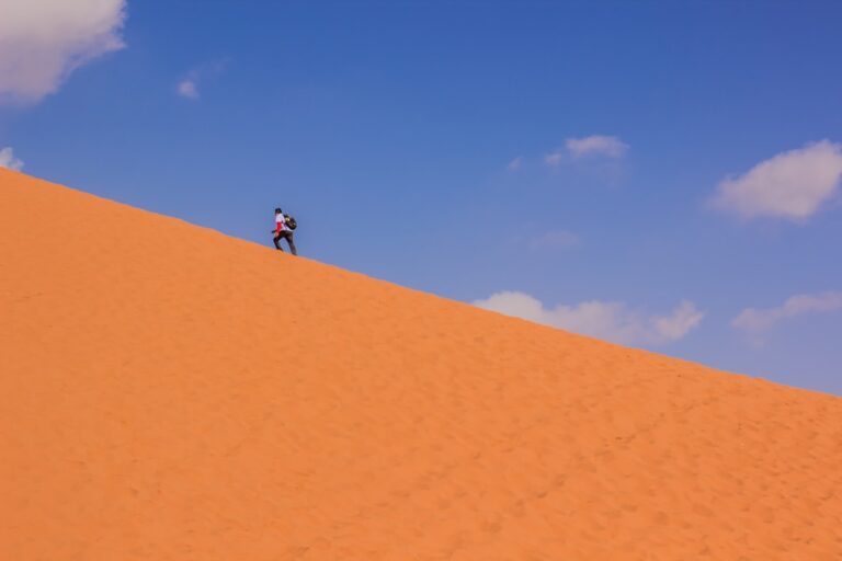 tourist hiking man desert sand dune hill horizon landscape scenic view yellow background in clear weather hot day time...
