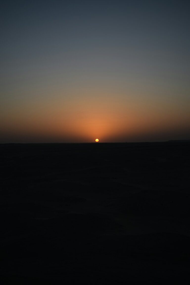 The sun is setting over the horizon of the ocean