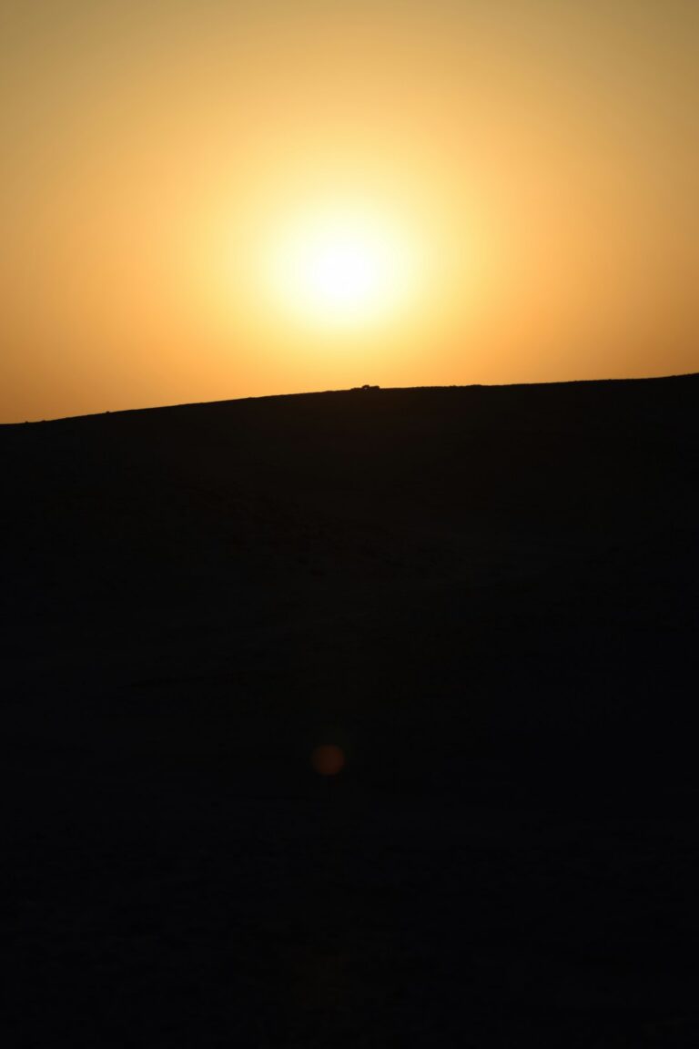 The sun is setting over the horizon of a desert