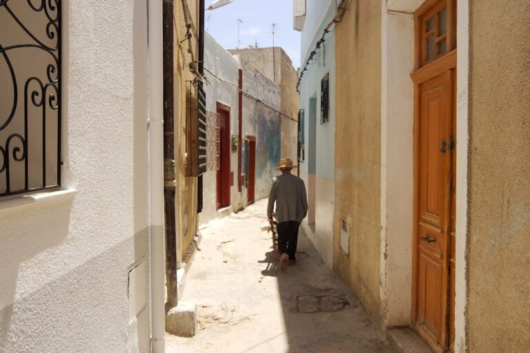 Person walks down a narrow, sunlit european street.