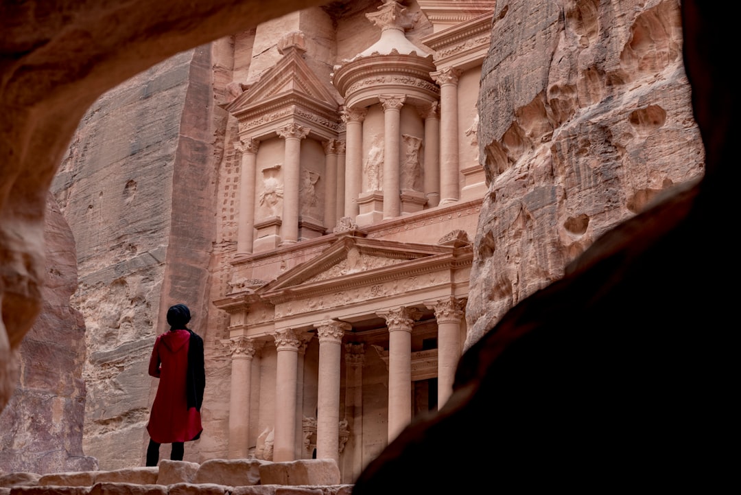woman in red coat standing in front of white concrete building during daytime