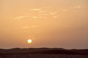 the sun is setting over the horizon of a desert