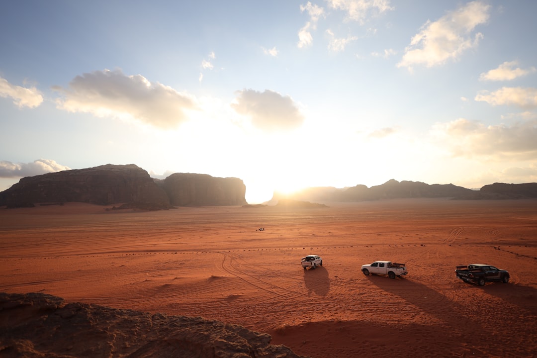 Three vehicles drive across a desert landscape at sunset.